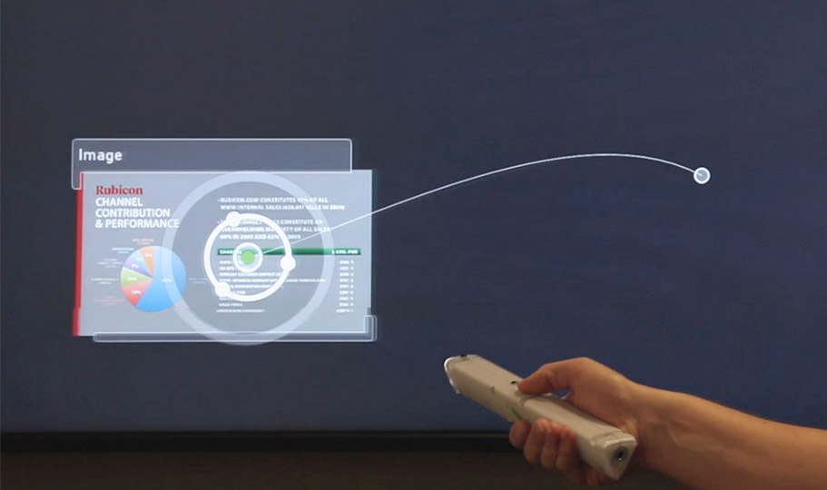 A hand points a gestural wand at a screen, controlling the size and placement of a slide in a presentation in Oblong's Mezzanine