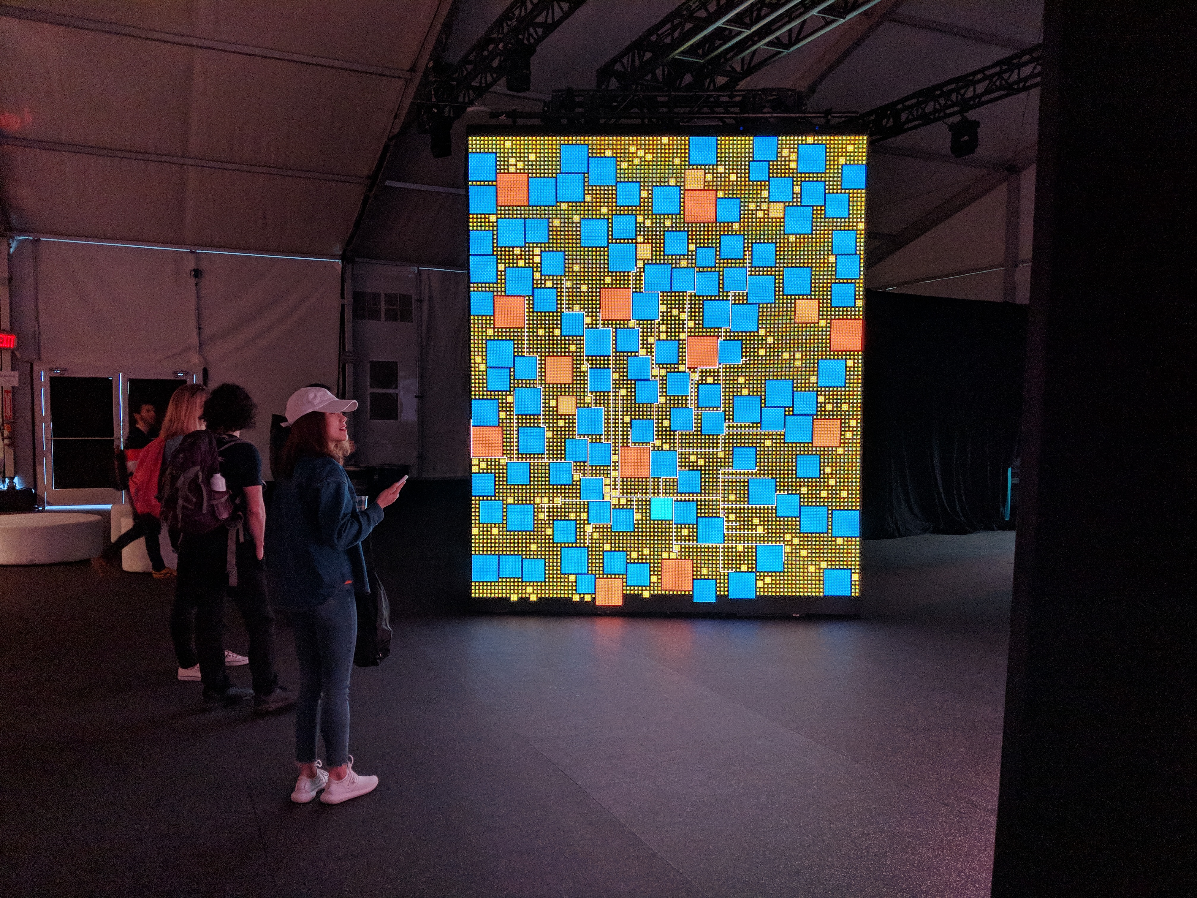 network view in People You May Know: a collection of blue, yellow, and orange squares in a grid with white lines between them on an 8ft tall screen with some onlookers