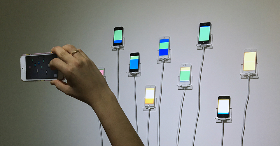 Gallery visitor takes a cellphone picture of infinite scroll, showing mounted iPhones on the phone's screen