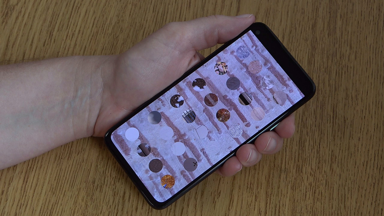 A mobile device in a person's hand shows an abstract interface reiminscent of a device's home screen, but with photos of physical objects and environments as options instead of apps.