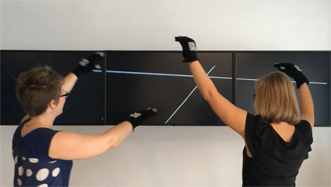 Two performers wearing gesture tracking gloves to draw virtual lines between their hands on a distant screen