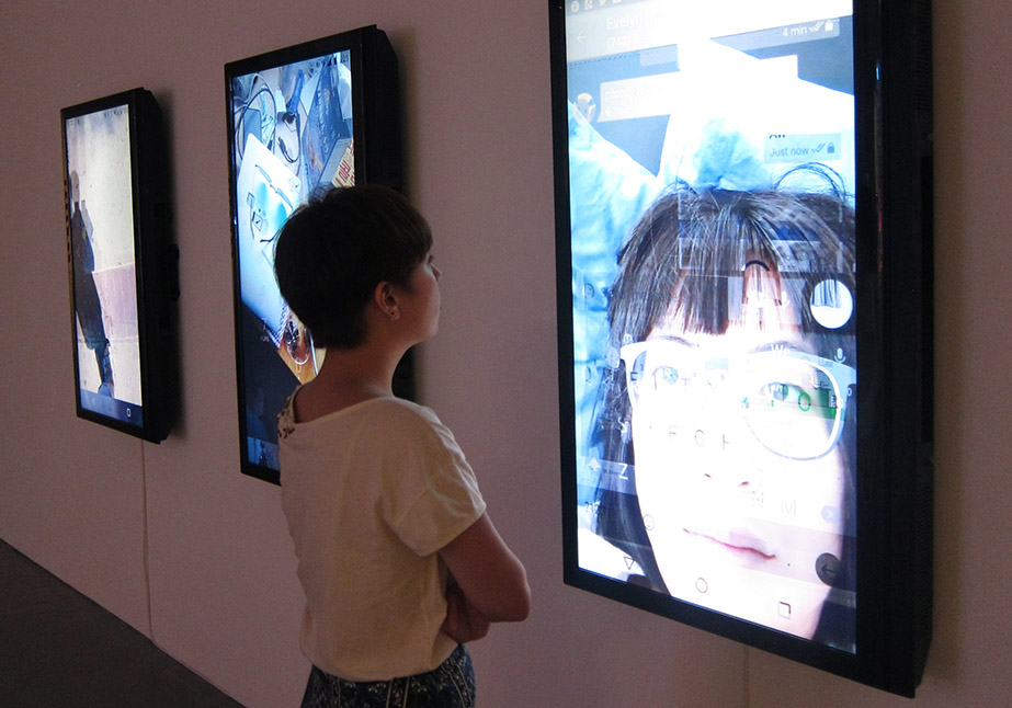 Woman examines a video collage portrait on a wall, showing a blend of a user's face, environment, and interface in user_is_present